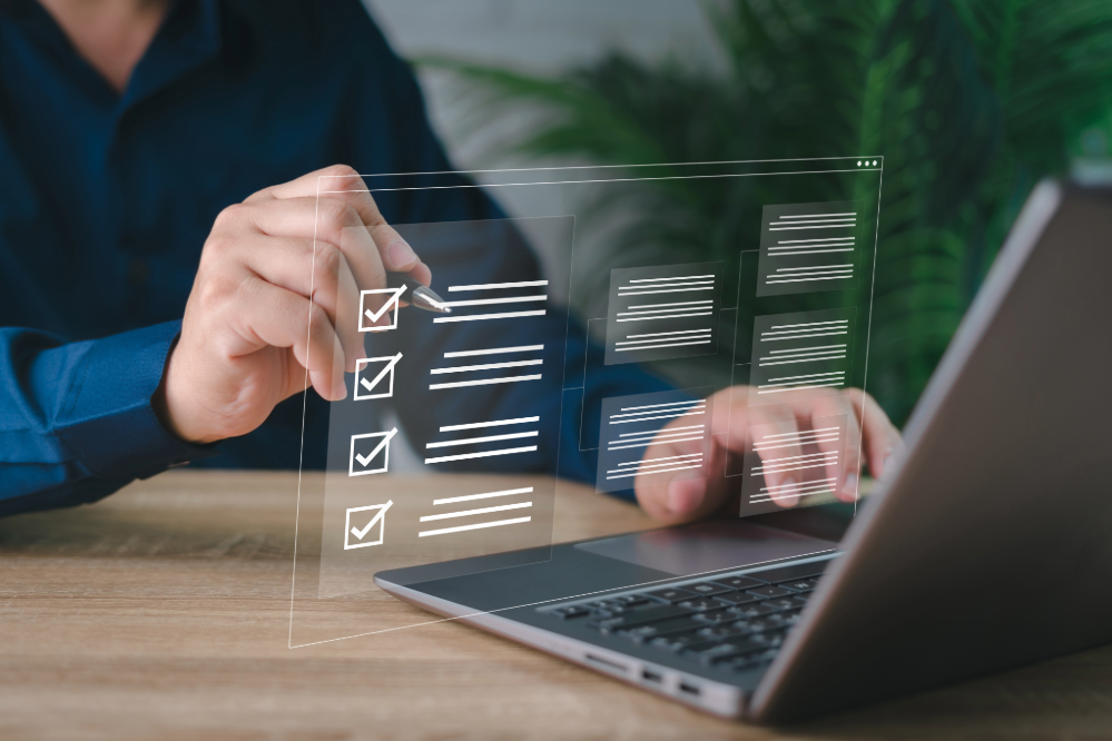 Close up of person typing on laptop looking over a checklist